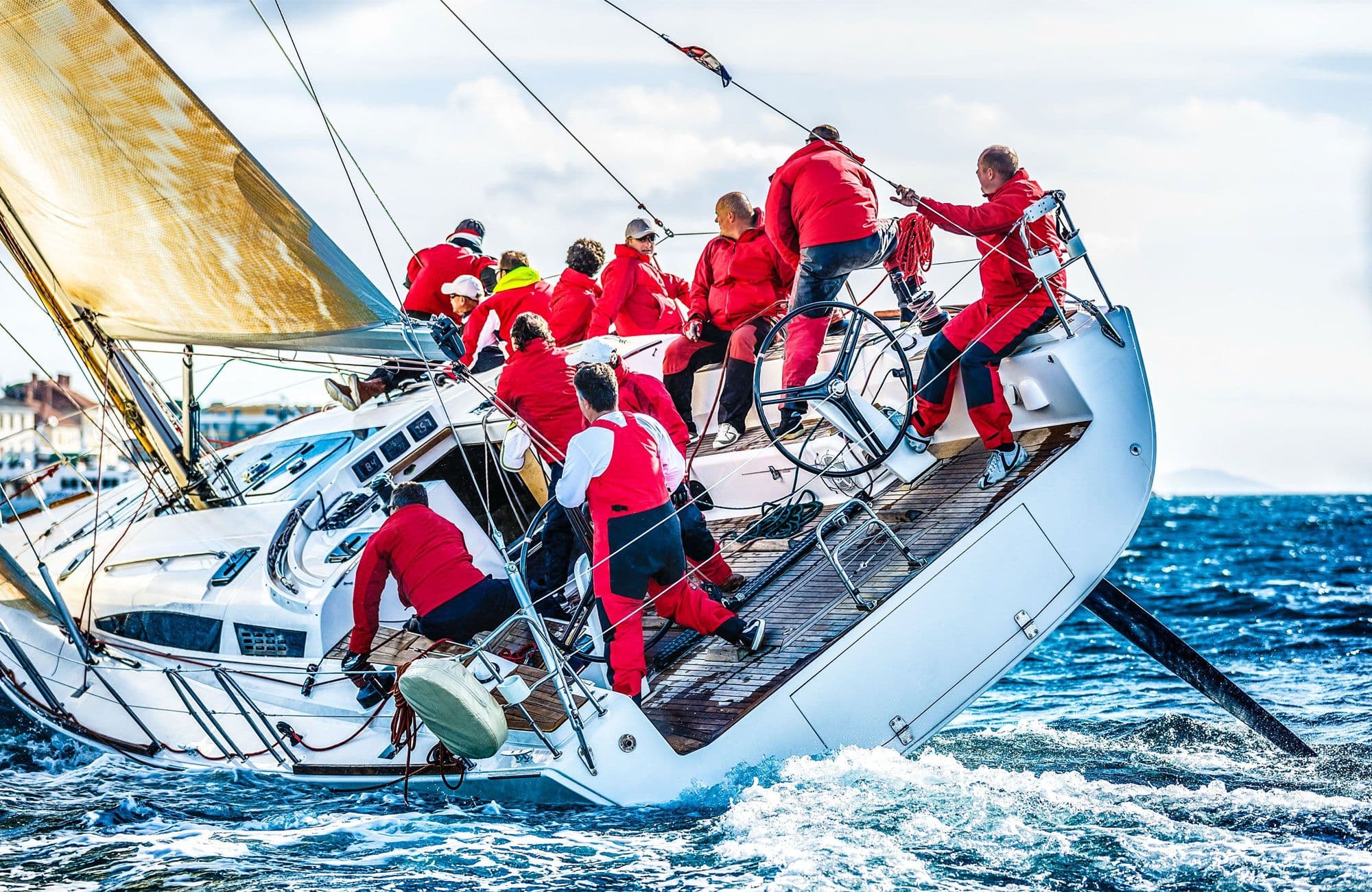 Team auf einer Segelyacht arbeitet gemeinsam an Deck und bedient Segel und Leinen bei starkem Wind auf offenem Meer.
